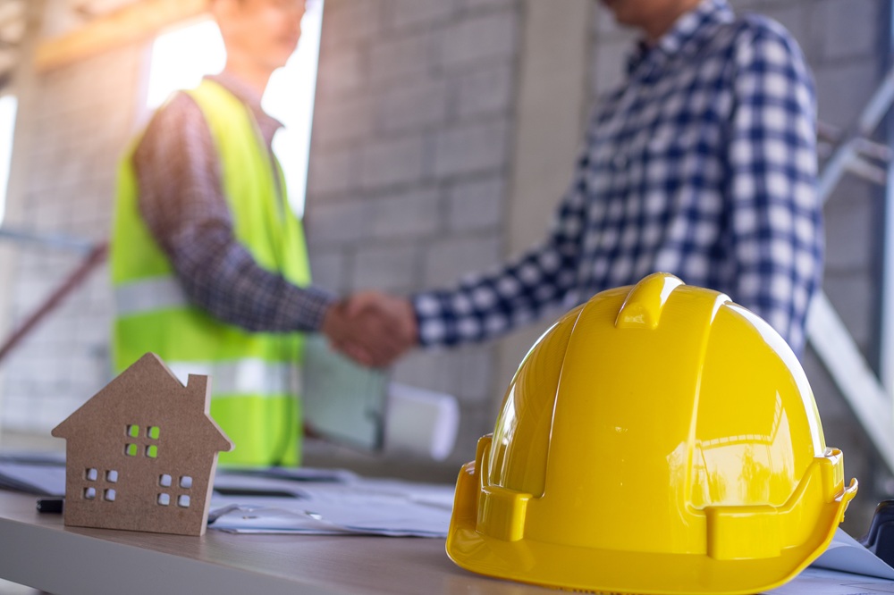 Two professionals shaking hands near hard hat and house model representing home remodeling consulting services – Home Remodeling Consulting